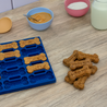 Blue silicone mold with bone-shaped dog treats on a wooden table with ingredients.