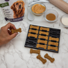 Dog biscuit making kit with ingredients and a hand holding a dog biscuit.