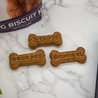 Dog biscuits with 'Good Boy' and 'Good Girl' text on a marble surface, next to a packaging label.